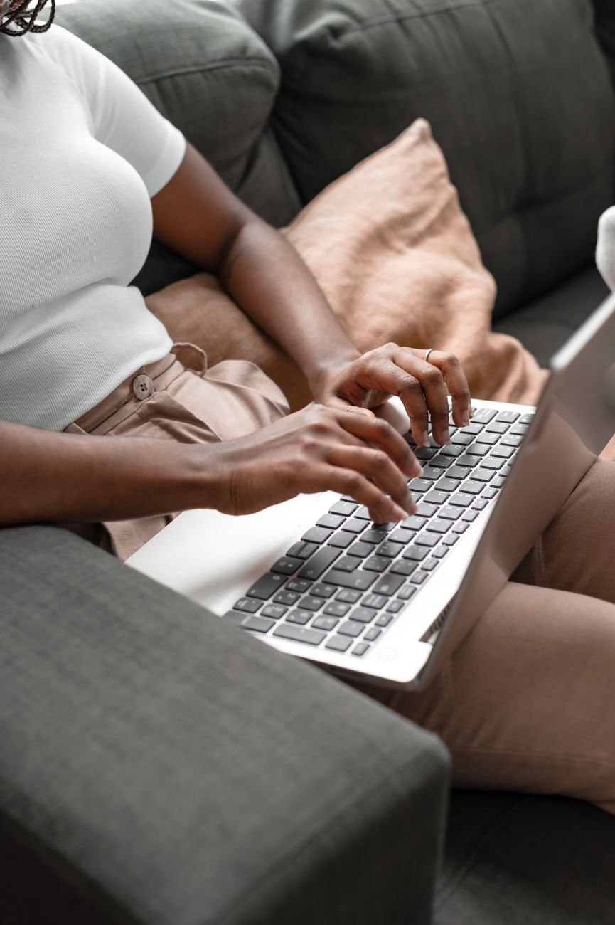 Woman sitting on sofa typing on laptop, comfortable home setting.